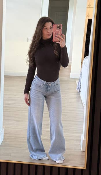 Person taking a reflector selfie wearing a fitted apical and wide-leg jeans, lasting successful a modern interior space