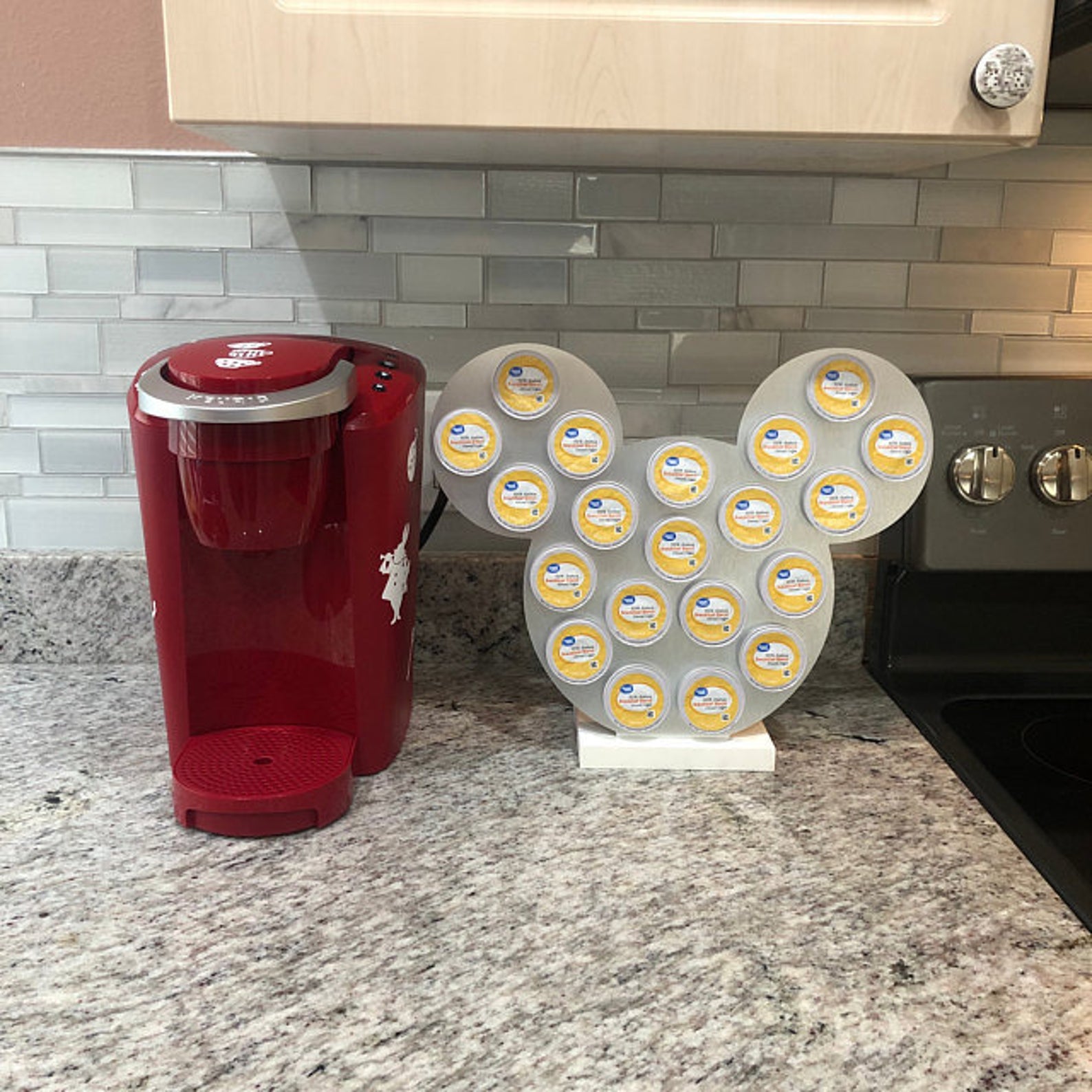 a silver mickey-shaped k-cup holder next to a keurig machine