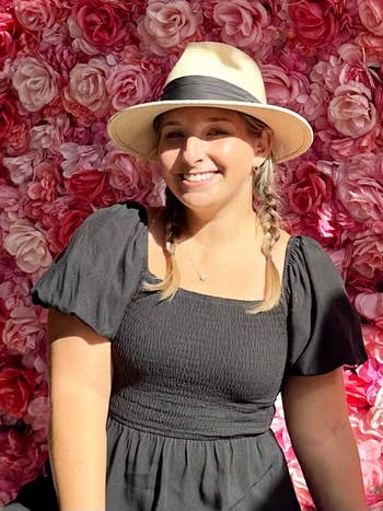 Woman in a hat smiles with a floral background, wearing a puffed-sleeve dress