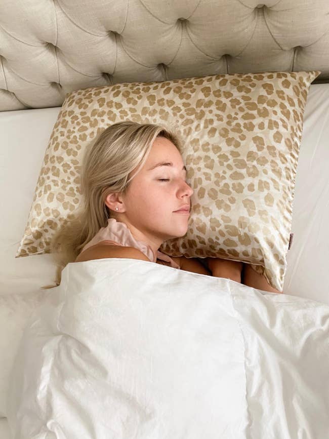 Woman resting on a leopard print pillowcase, white duvet, eyes closed