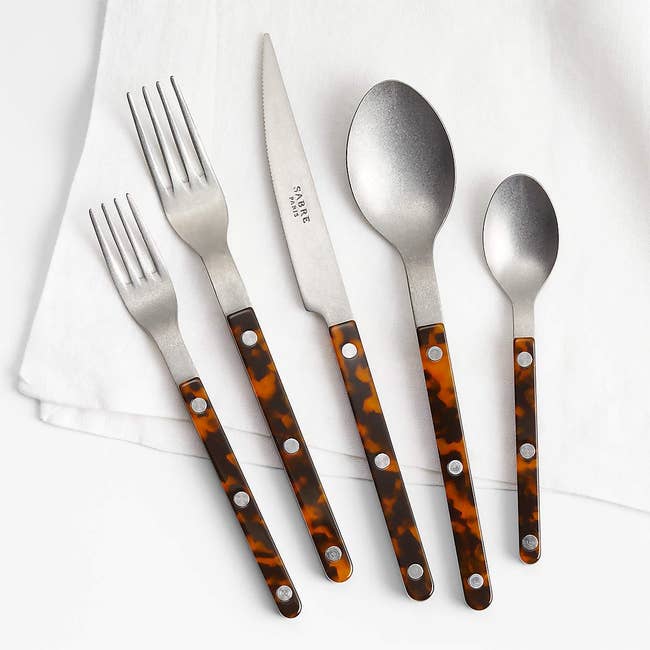 A set of silverware with tortoiseshell-patterned handles, including two forks, a knife, and two spoons