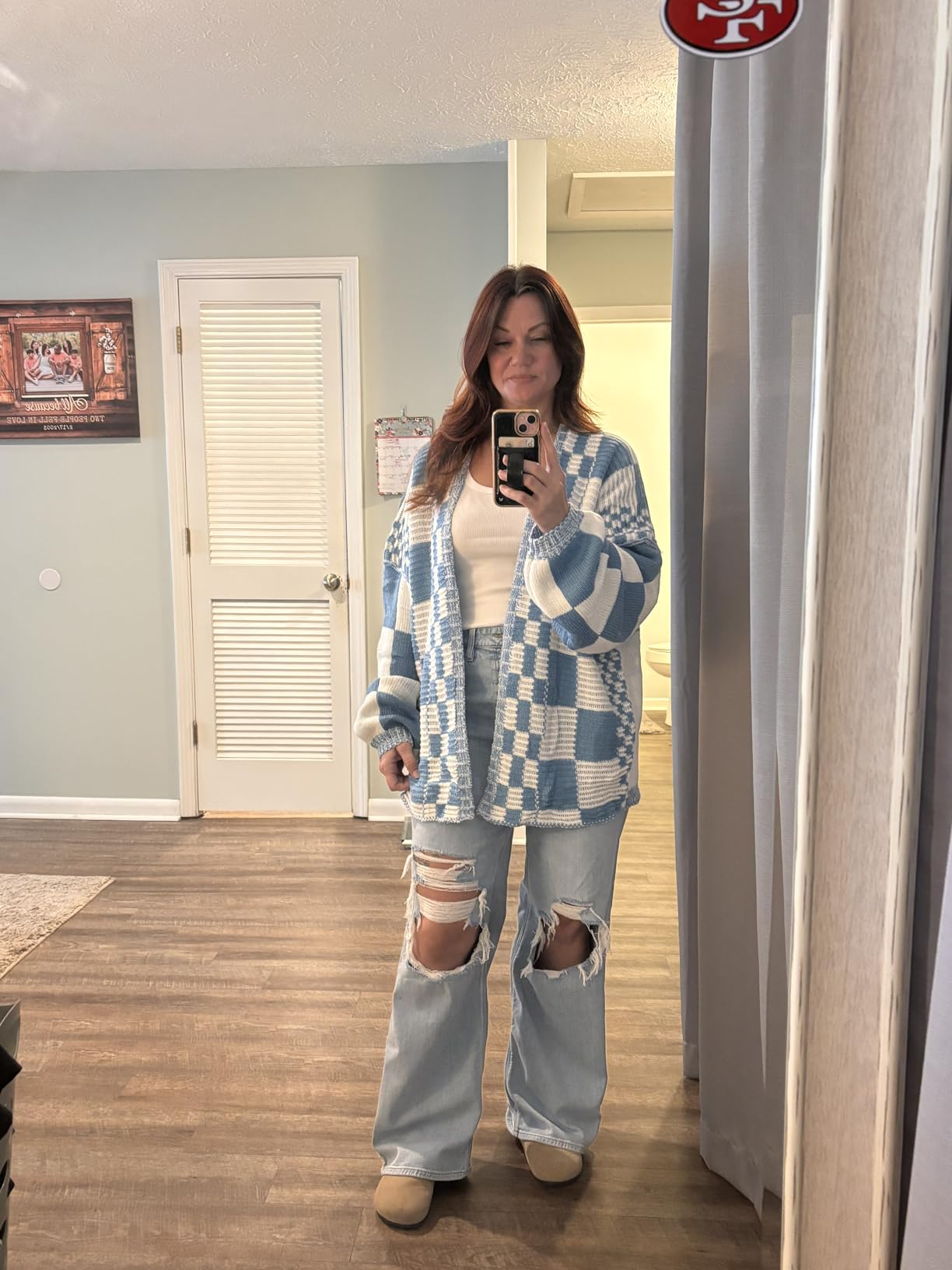 Person taking a reflector  selfie wearing a checkered cardigan, achromatic  top, ripped jeans, and beige shoes successful  a casual location  setting