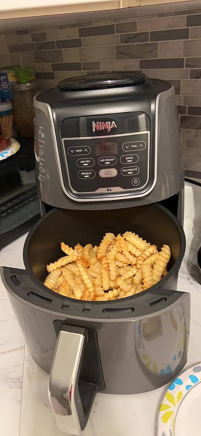 a reviewer's air fryer on a kitchen counter with crinkle-cut fries inside