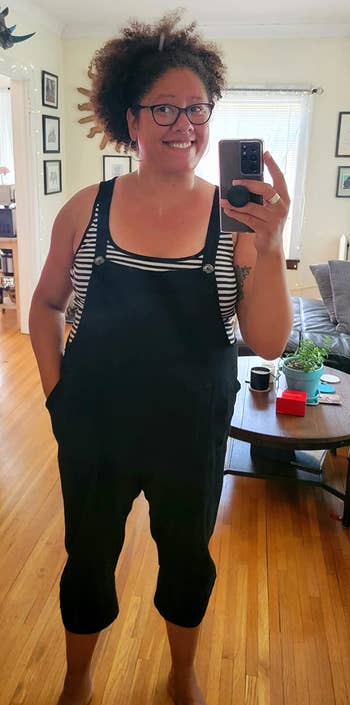 a reviewer wearing the overalls in black over a striped tank top 