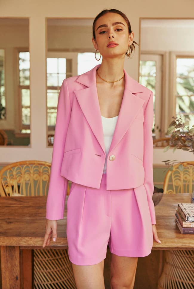 model in a pink blazer and shorts stands indoors, fashionably dressed for a shopping editorial