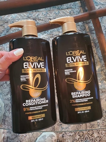 reviewer photo of them holding a brown bottle of conditioner next to a matching bottle of shampoo