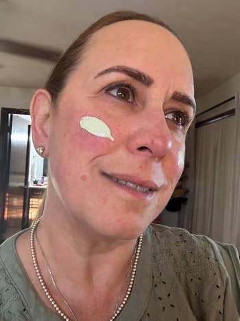 A idiosyncratic with moisturizing pick applied to their cheek, wearing an embroidered apical and pearl necklace