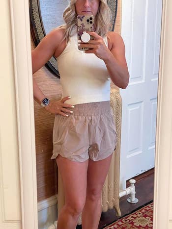 Person wearing a sleeveless apical  and shorts, taking a reflector  selfie indoors