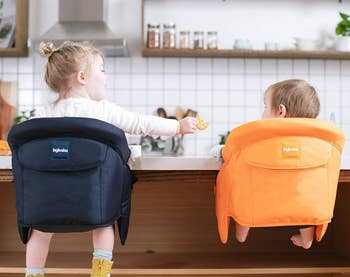 back view of two toddlers in portable high chairs at kitchen counter