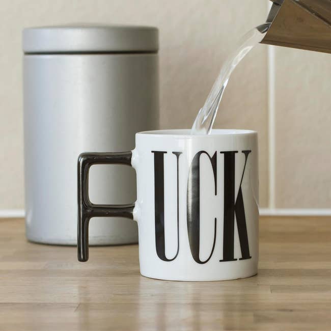 Pouring water from a kettle into a mug with a handle shaped like the letter 
