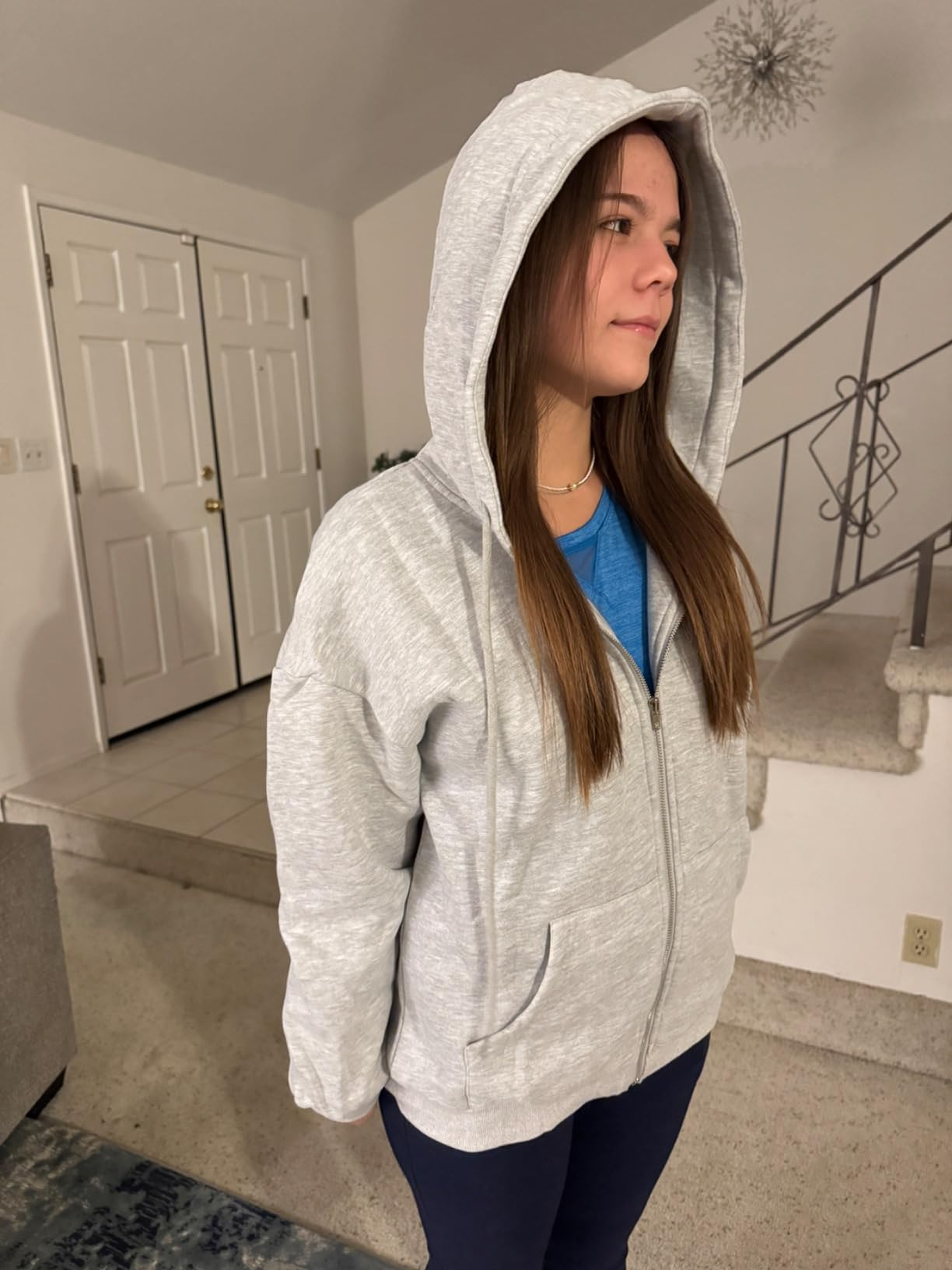 Person wearing a casual grey  hoodie and bluish  shirt, lasting  indoors. The hoodie is zipped up, with the hood connected  their head