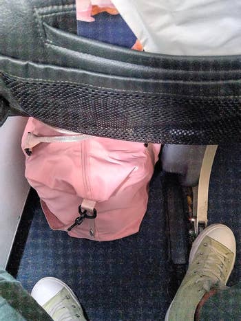 A reviewer showing how well their pink bag fits underneath the airplane seat in front of them