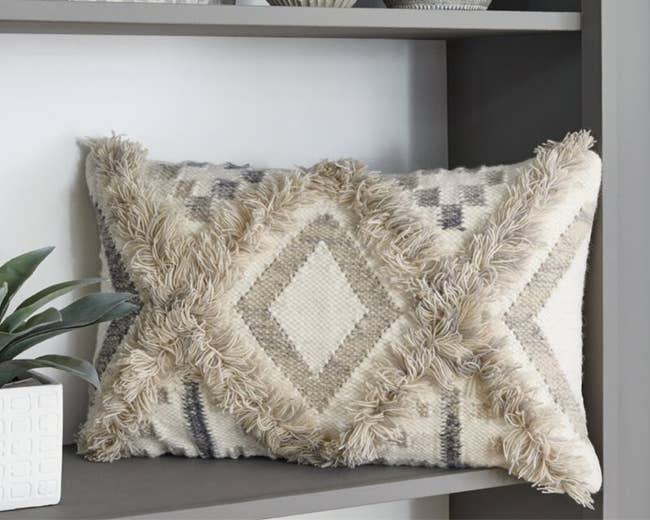 A beige and grey pillow with fringe 