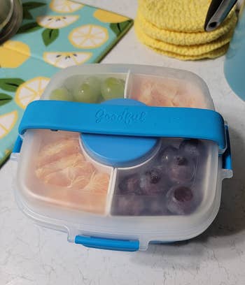 A lunchbox with separate compartments containing grapes, sandwiches, and berries