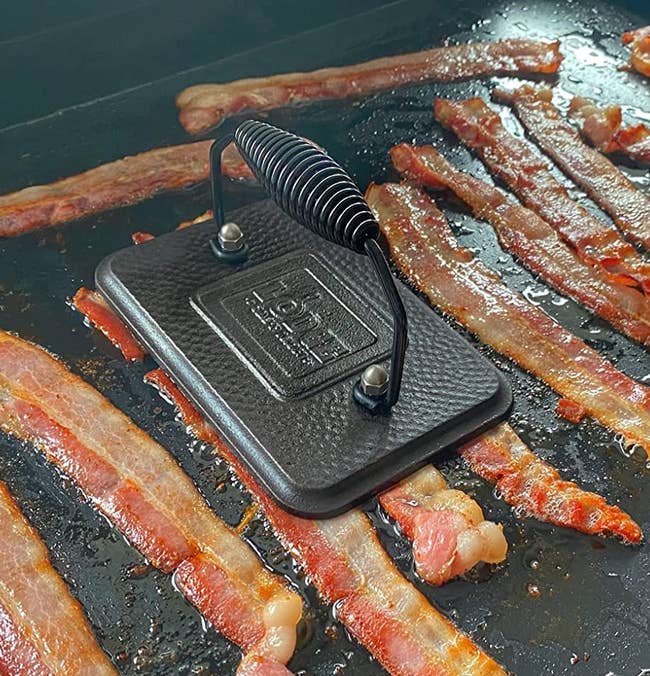 reviewer photo of the grill press on top of bacon that's cooking on a griddle