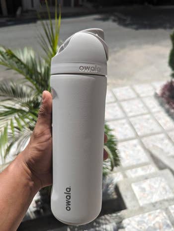 Person holding a matte-textured Owala water bottle outdoors, featuring a flip-open lid design, likely for a shopping article on reusable bottles