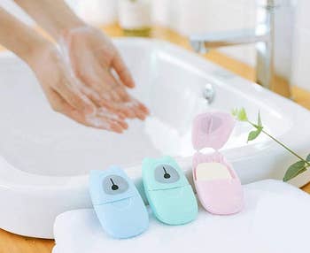 person washing hands at sink with three portable soap sheet containers on the counter