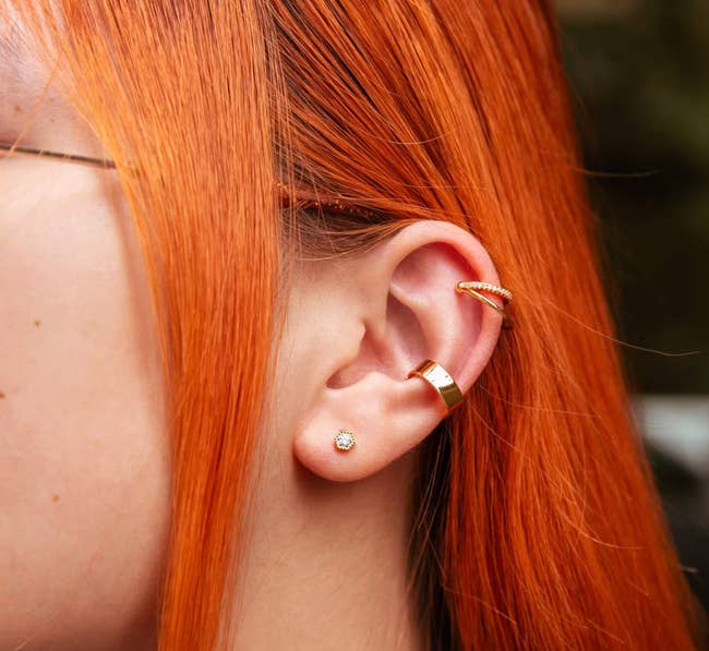 Close-up of a person's ear with three gold earrings, article related to jewelry shopping