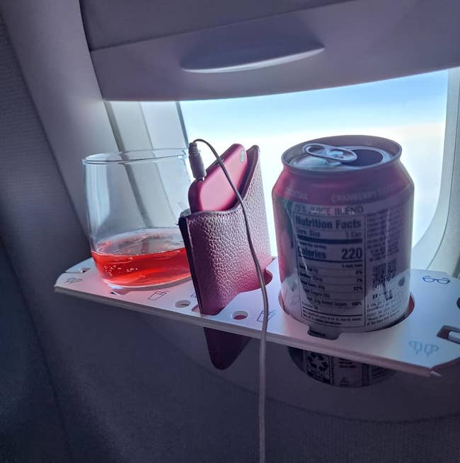 a reviewer image of the BevLedge holding a can, a glass of wine, and a charging cellphone 