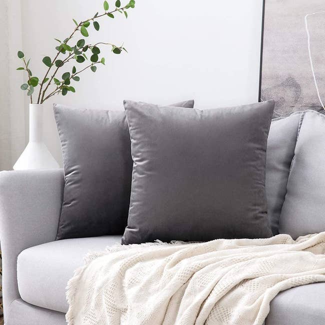 two throw pillows on a couch with dark gray covers on them