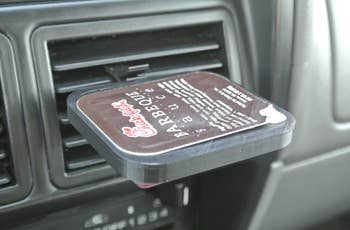 Close up of a container of barbecue sauce in the single clip holder attached to a car vent