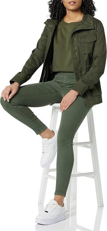 Orang dalam pakaian kasual dengan jaket, jegging hijau tentara, dan sepatu kets, duduk di bangku