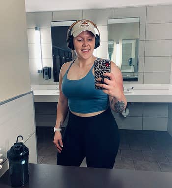 another reviewer wearing the teal tank top in a gym bathroom