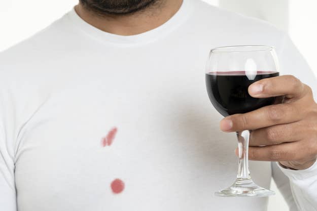 A person holding a glass of red wine has spilled some on their white shirt