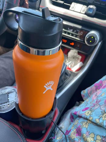 another reviewer's orange Hydro Flask in the car cup holder using the extender