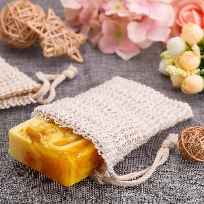 A bar of soap in a cream colored textured pouch with tie closures on top 