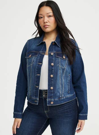 Person modeling a denim overgarment with fastener details implicit a achromatic top, styled with acheronian jeans