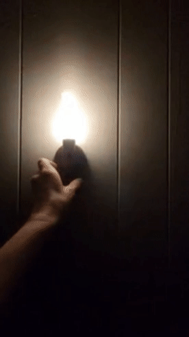 reviewer removing the lit sconce from its wall holder in a dark room