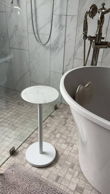 Bathroom with a walk-in solid shower, a freestanding tub, and a tiny circular broadside table. Marble and tiled surfaces make a modern look