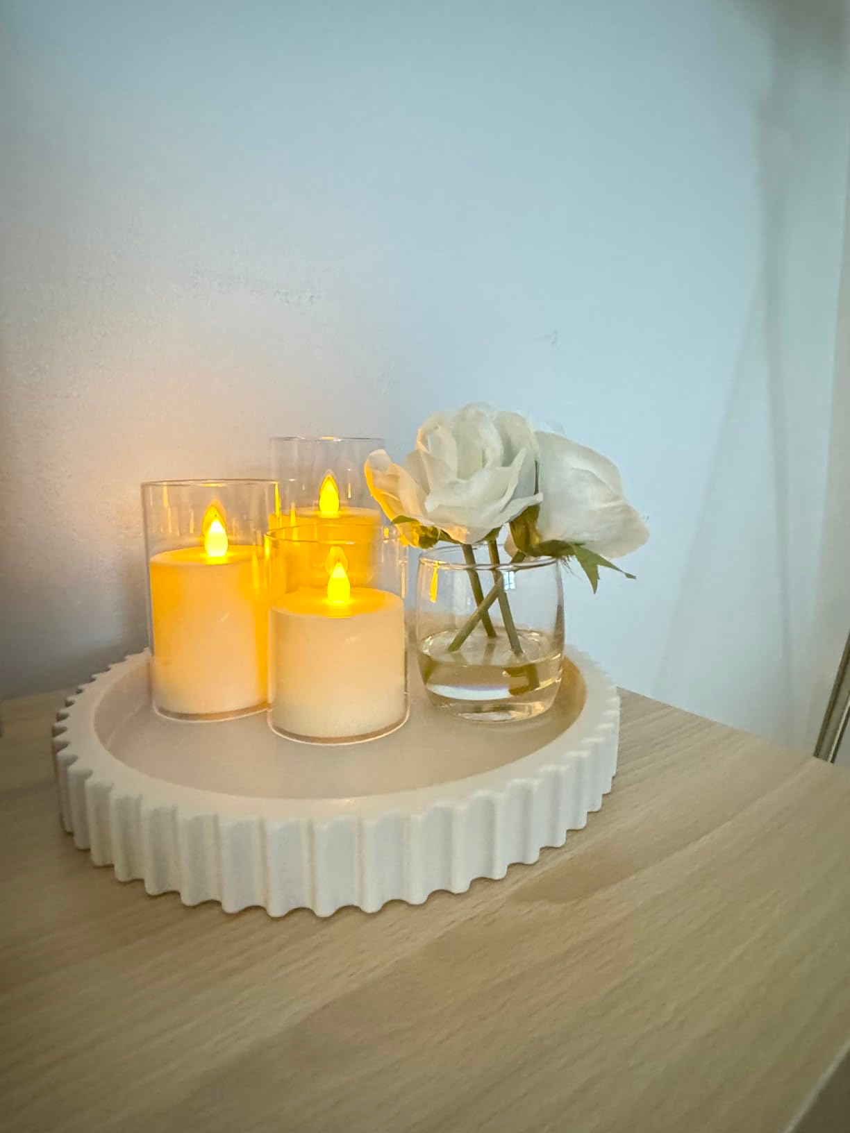 A acceptable   of flameless candles and a azygous  achromatic  roseate  successful  a tiny  solid  vase connected  a airy  woody  surface, creating a cozy atmosphere