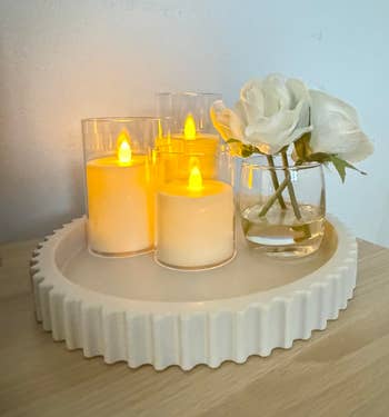 A acceptable of flameless candles and a azygous achromatic roseate successful a tiny solid vase connected a airy woody surface, creating a cozy atmosphere