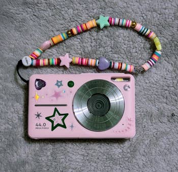 A pastel-colored artifact  camera with prima  and bosom  decorations connected  a plush surface. It has a colorful beaded strap