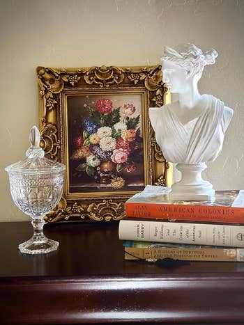 the bust displayed on top of a stack of books next to a framed painting