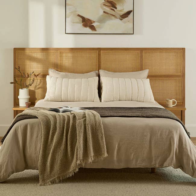 Elegantly made-up bed with neutral-toned linens and a textured throw blanket, set against a cane headboard