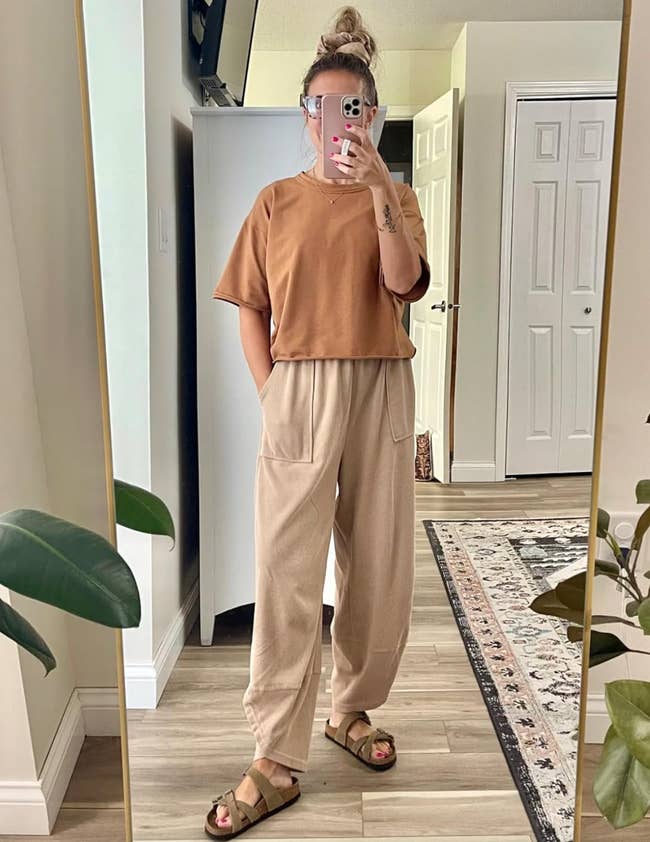 Person wearing casual oversize apical  and escaped   pants, with sandals, taking a reflector  selfie successful  a cozy room