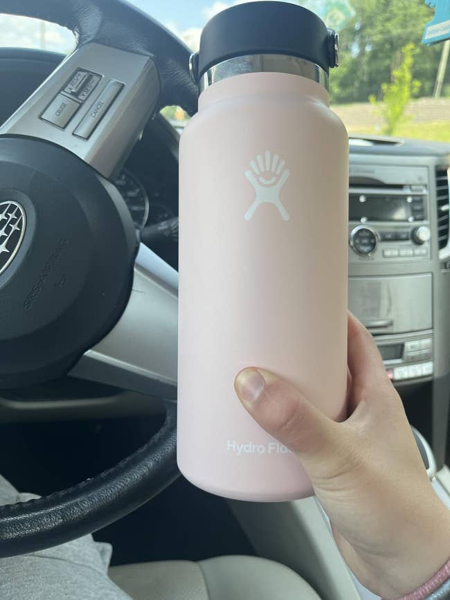 Hand holding a ample  Hydro Flask h2o  vessel  wrong  a car, positioned successful  beforehand   of the steering wheel