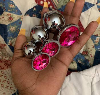 Reviewer holding three metal butt plugs with pink gemstones