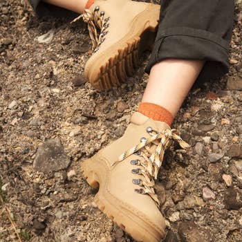A person wearing beige hiking boots and dark pants sitting on rocky ground