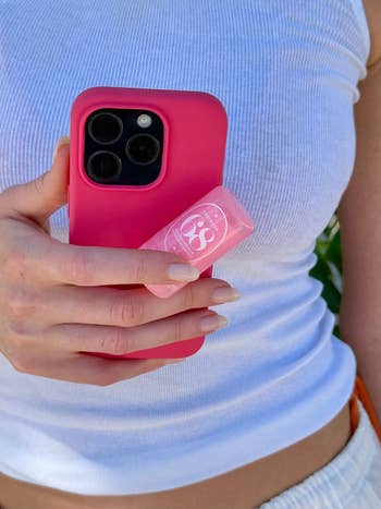 Person holding a pinkish  smartphone lawsuit  and a tiny  conduit  of perfume balm against a achromatic  ribbed vessel  top