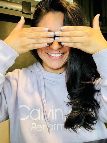 Person in a Calvin Klein hoodie, covering eyes with hands showing off manicured nails