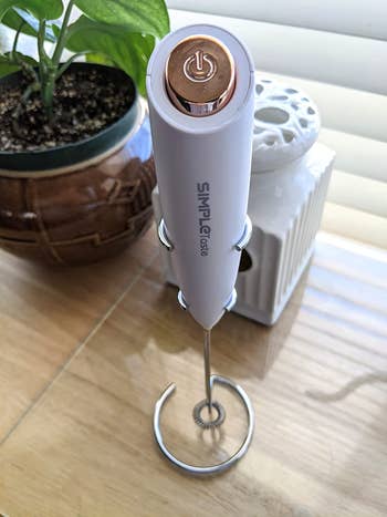 Reviewer image of white frother with silver power button on top of handle, standing wooden table
