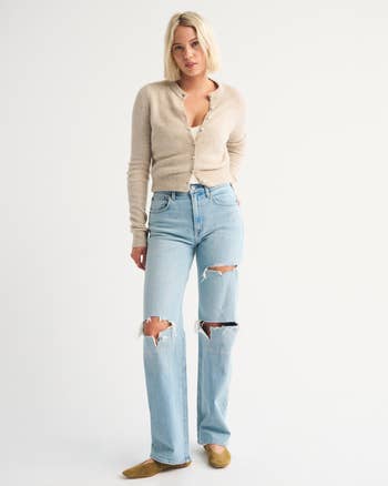 Person wearing a button-up cardigan, ripped jeans, and casual shoes successful  a workplace  setting. Ideal for casual benignant   buying  content