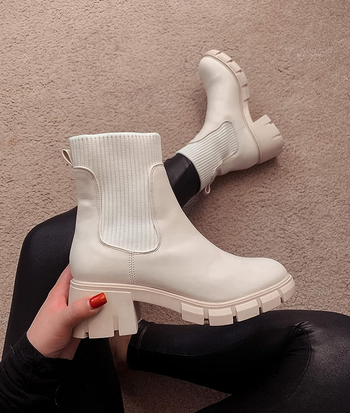 reviewer wearing and holding up one of the white boots