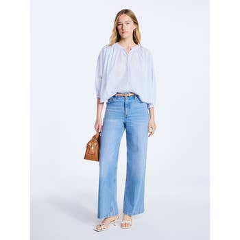 Person wearing a loose blouse, wide-leg jeans, and sandals, holding a small handbag; casual outfit for a shopping-themed article