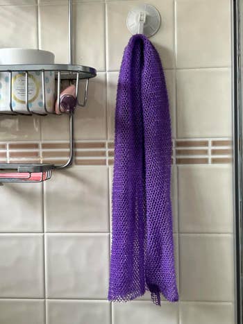Purple mesh bath cloth hanging on a tile wall near a shower caddy, suggesting a bathroom shopping theme