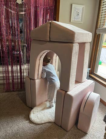 reviewer's child playing inside fort made with stacked cushions